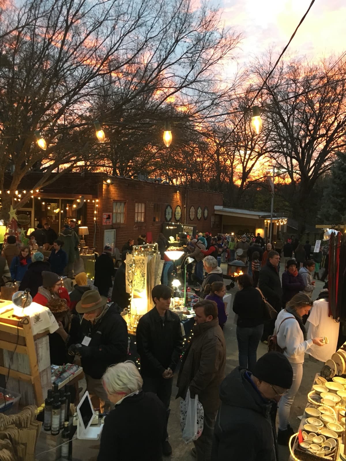 The market courtyard glowing at sunset, shoppers gathered around artist tables and a fire